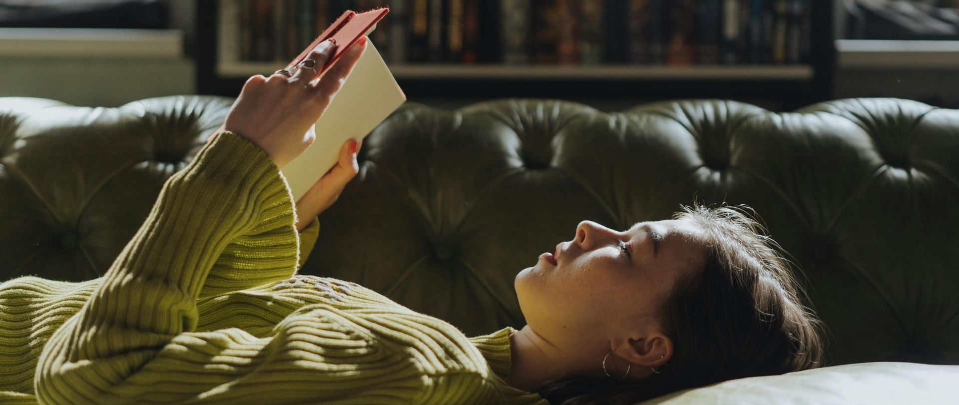 A young woman lies on a sofa reading a book, enjoying a peaceful indoor moment.